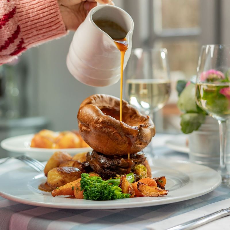 Sunday roast plated with gravy being poured slowly over the giant yorkshire pudding